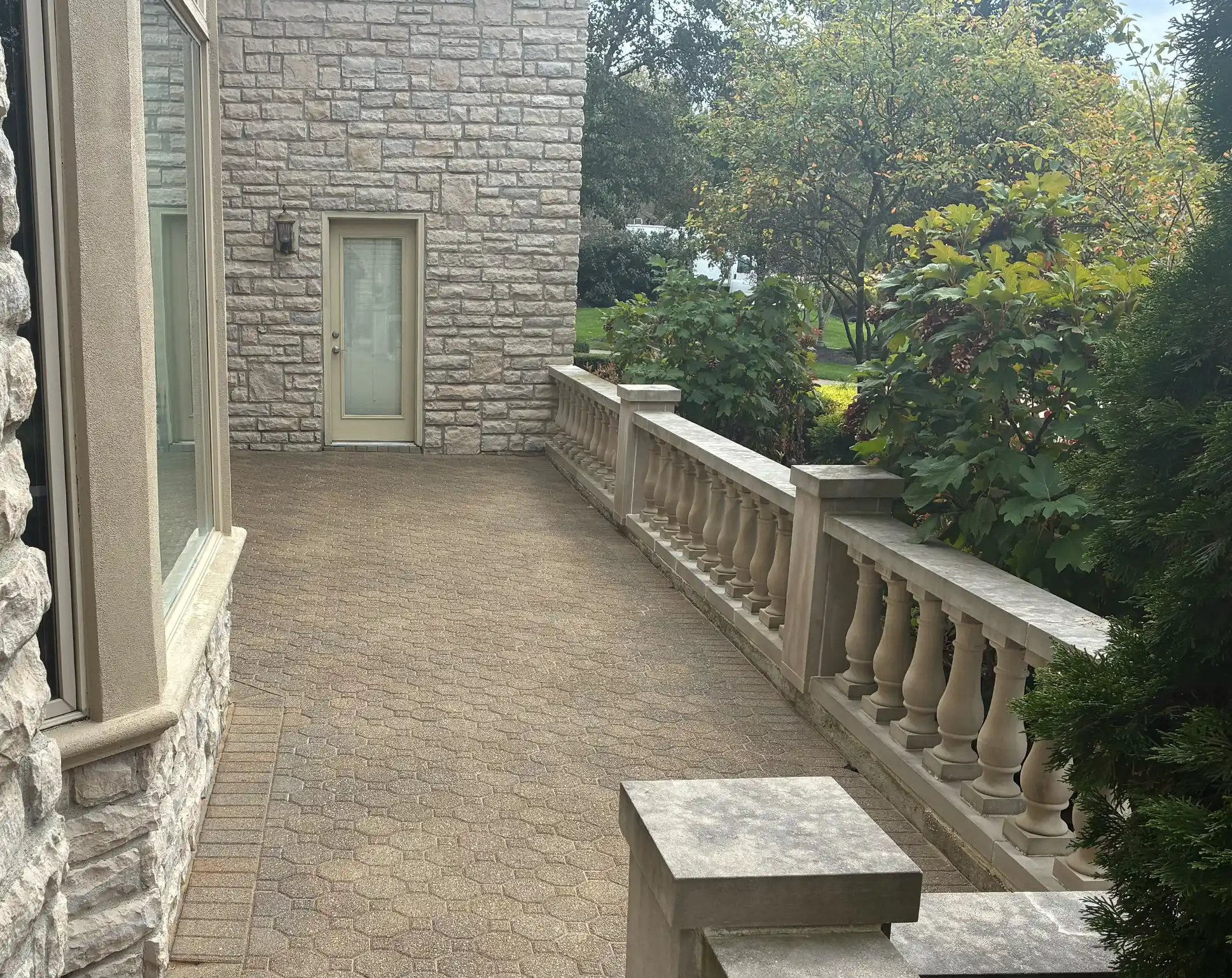 Outdoor patio area featuring a stone wall house, decorative railing, and landscaped greenery, highlighting a restored paver surface.