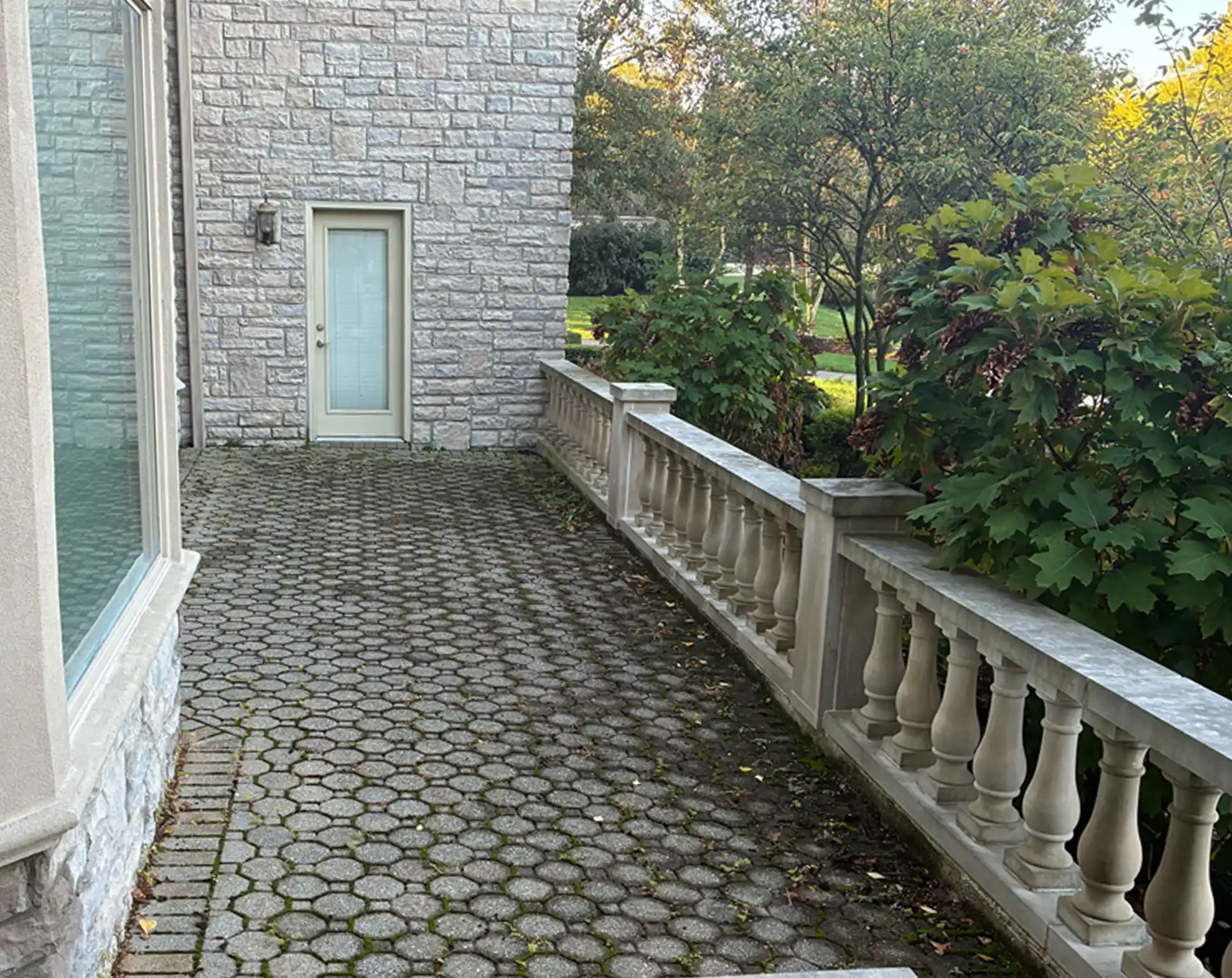 Paver walkway leading to a door, surrounded by a stone wall and greenery, illustrating potential outdoor restoration projects by Perfect Paver Co.