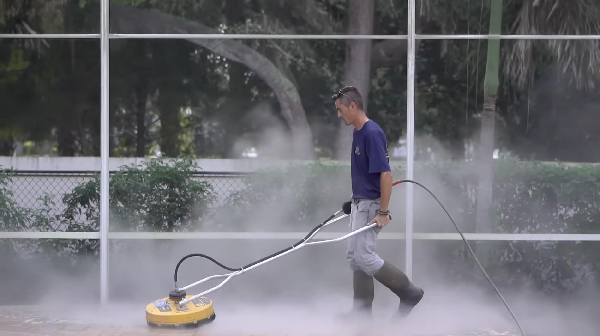 Technician using a pressure washer on pavers, surrounded by mist, demonstrating professional cleaning techniques for paver restoration.