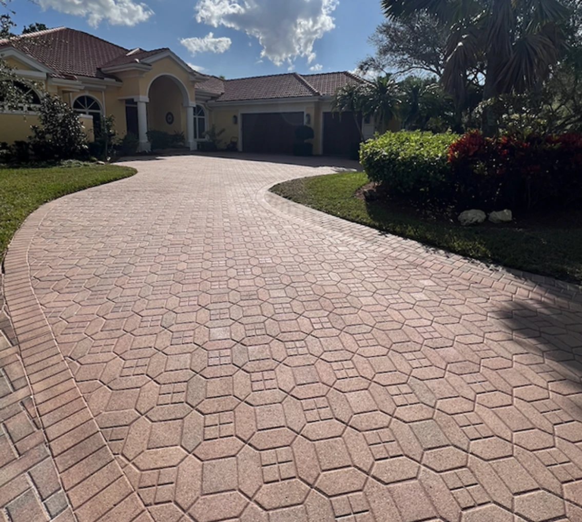 Curved driveway with newly tinted pavers, showcasing a vibrant, restored finish, surrounded by lush greenery and a residential home, illustrating the benefits of paver tinting services by Perfect Paver Co.